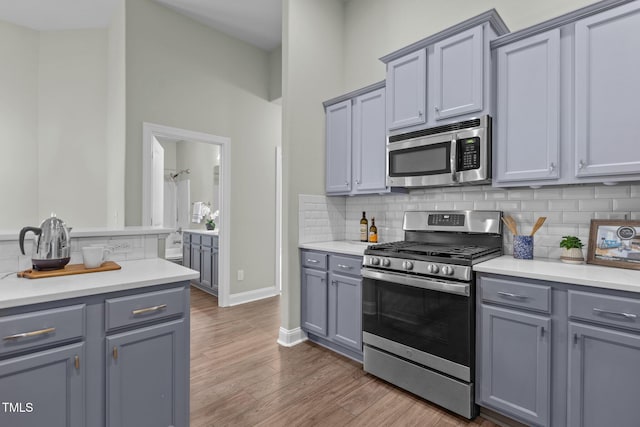 kitchen with stainless steel appliances, dark wood-style flooring, light countertops, gray cabinets, and backsplash