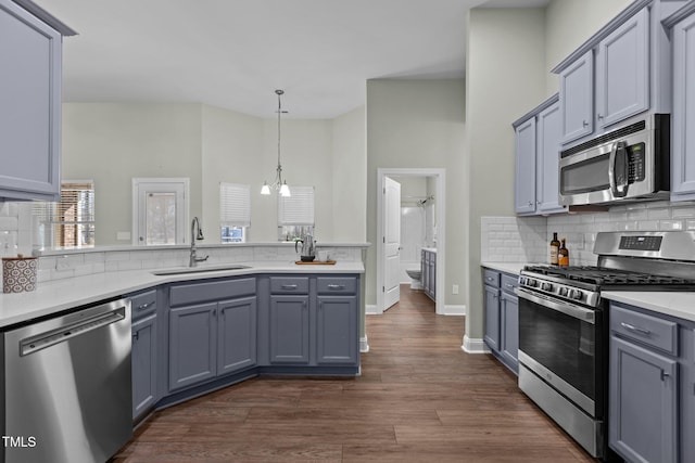 kitchen with a sink, light countertops, appliances with stainless steel finishes, decorative backsplash, and pendant lighting