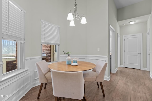 dining space with light wood-style floors, a wainscoted wall, a decorative wall, and an inviting chandelier