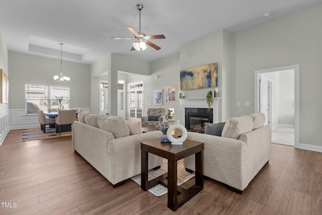 living area with a glass covered fireplace, a towering ceiling, wood finished floors, a tray ceiling, and a decorative wall