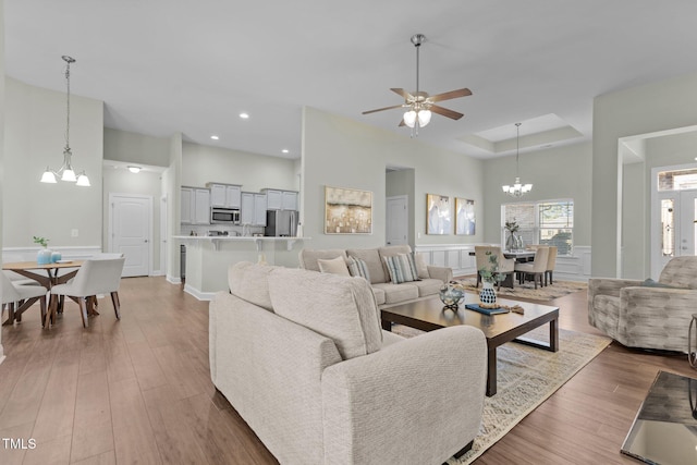 living area featuring a tray ceiling, recessed lighting, a high ceiling, wood finished floors, and ceiling fan with notable chandelier