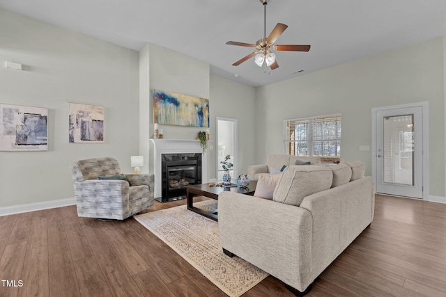 living room with visible vents, baseboards, a glass covered fireplace, ceiling fan, and wood finished floors