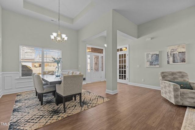 dining room with a tray ceiling, a decorative wall, an inviting chandelier, wainscoting, and wood finished floors