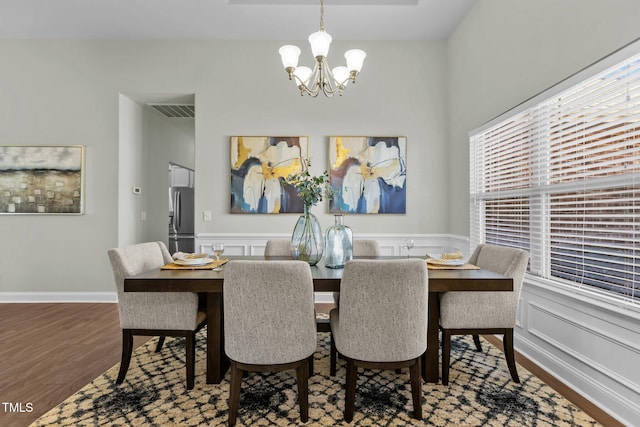 dining area featuring a decorative wall, a wainscoted wall, a notable chandelier, wood finished floors, and visible vents