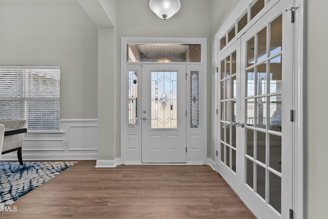 foyer with french doors, a wainscoted wall, a decorative wall, and wood finished floors