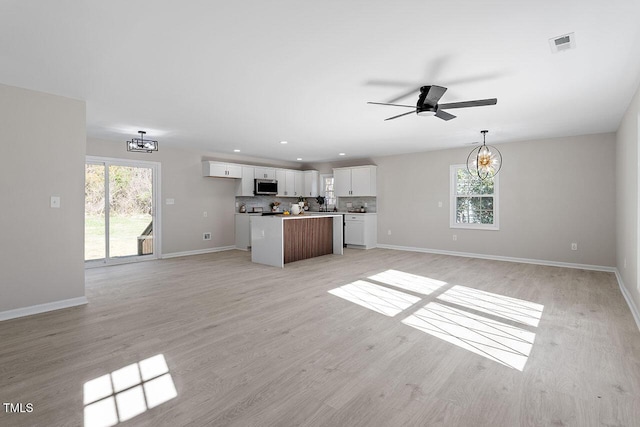 unfurnished living room with ceiling fan with notable chandelier and light wood-type flooring