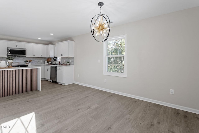 kitchen with a chandelier, appliances with stainless steel finishes, white cabinets, decorative light fixtures, and backsplash