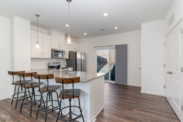 kitchen featuring stainless steel appliances, a sink, white cabinets, hanging light fixtures, and light stone countertops