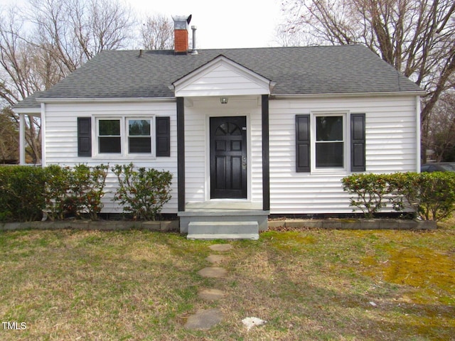 view of front facade with a front lawn, roof with shingles, and a chimney