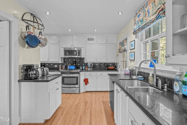 kitchen featuring stainless steel appliances, decorative backsplash, white cabinets, light hardwood / wood-style flooring, and sink