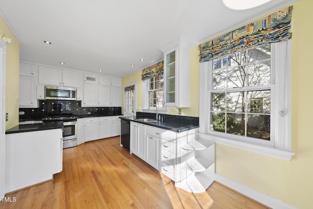 kitchen featuring appliances with stainless steel finishes, sink, light wood-type flooring, white cabinetry, and decorative backsplash