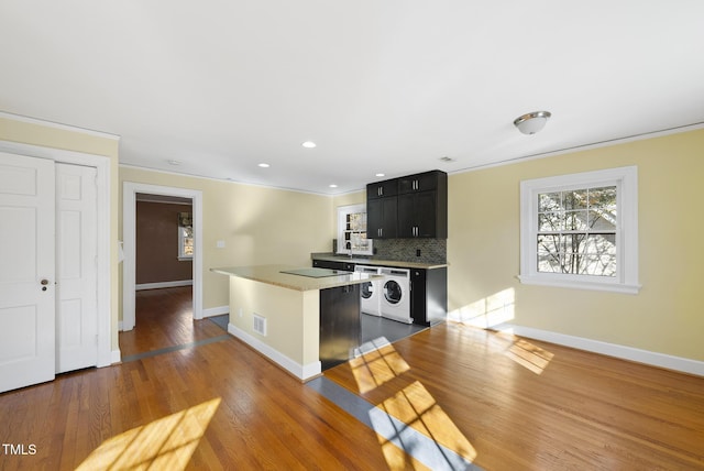 kitchen featuring crown molding, independent washer and dryer, dark wood-type flooring, and decorative backsplash