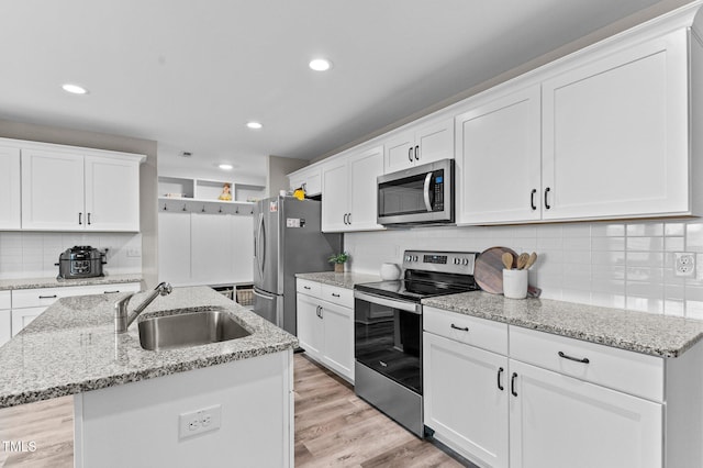 kitchen featuring appliances with stainless steel finishes, white cabinetry, sink, a kitchen island with sink, and light stone counters