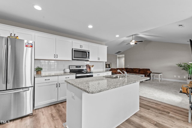 kitchen with sink, white cabinetry, stainless steel appliances, light stone counters, and an island with sink