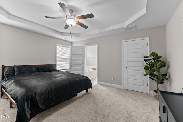 bedroom featuring a raised ceiling, connected bathroom, light colored carpet, and ceiling fan