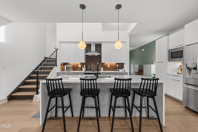 kitchen with wall chimney range hood, sink, appliances with stainless steel finishes, white cabinetry, and hanging light fixtures