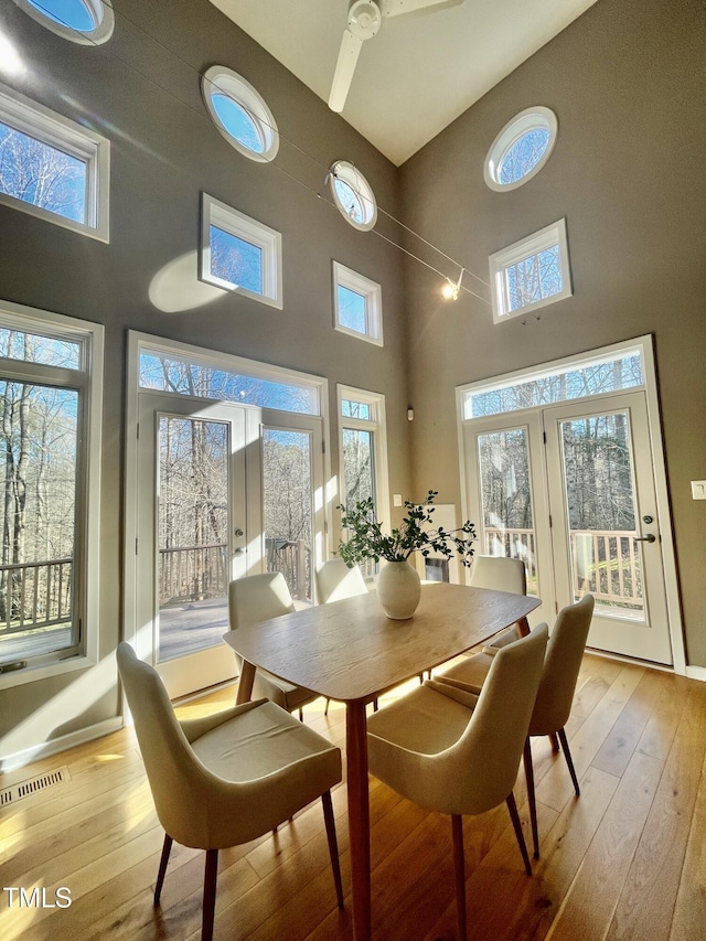 dining room with a high ceiling, light wood-type flooring, ceiling fan, and french doors