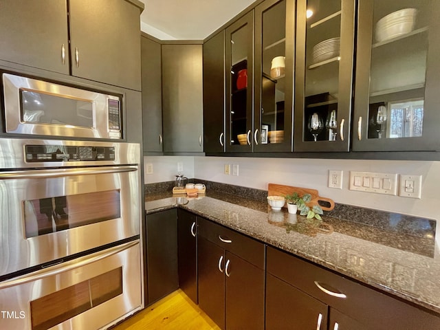 kitchen with stainless steel appliances, light wood-type flooring, dark stone counters, and dark brown cabinetry