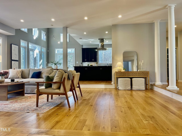 living room featuring high vaulted ceiling, light wood-type flooring, and ornate columns