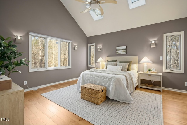 bedroom with ceiling fan, a skylight, high vaulted ceiling, and light hardwood / wood-style floors