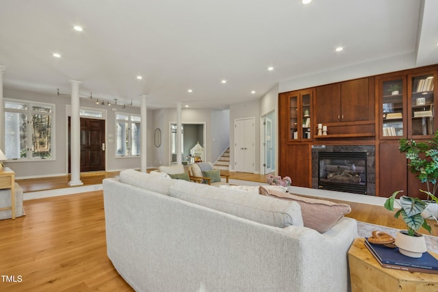 living room with a high end fireplace, light wood-type flooring, rail lighting, and ornate columns