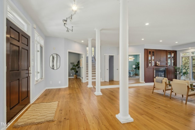 entrance foyer featuring track lighting, light hardwood / wood-style floors, and ornate columns