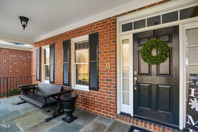 doorway to property featuring a porch and brick siding