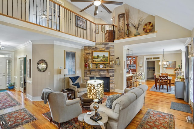 living room with light wood-style floors, baseboards, ornamental molding, and a stone fireplace