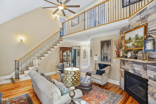 living room featuring stairs, a stone fireplace, baseboards, and wood finished floors