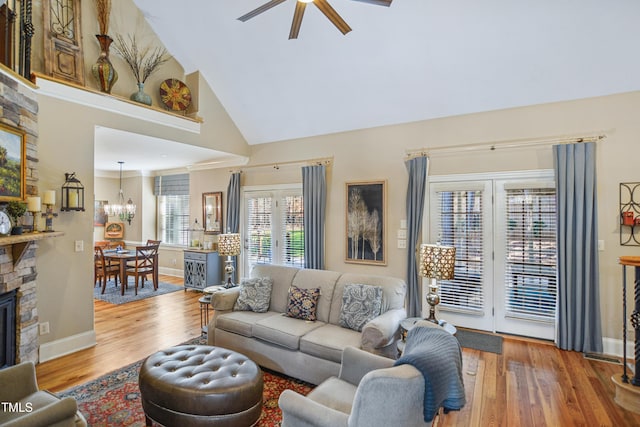 living area with high vaulted ceiling, ceiling fan with notable chandelier, a fireplace, and wood finished floors