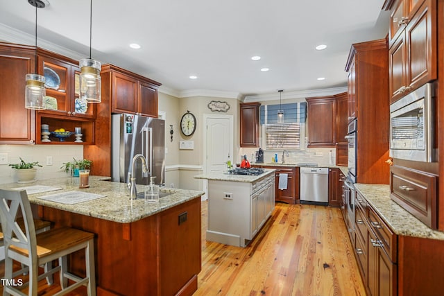 kitchen featuring light wood finished floors, appliances with stainless steel finishes, ornamental molding, a peninsula, and a sink