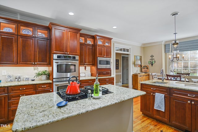 kitchen with crown molding, a center island with sink, light wood-style flooring, appliances with stainless steel finishes, and a sink