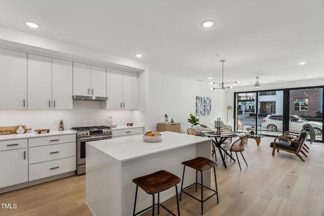 kitchen featuring gas range, white cabinets, a kitchen island, light wood-type flooring, and pendant lighting