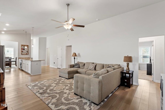 living room with high vaulted ceiling, baseboards, ceiling fan, and light wood finished floors