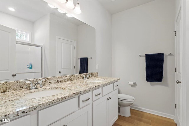 full bath with double vanity, wood finished floors, a sink, and toilet