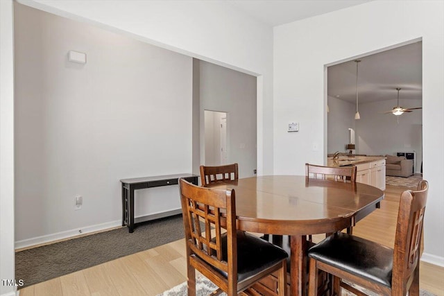 dining space featuring light wood finished floors, a ceiling fan, and baseboards