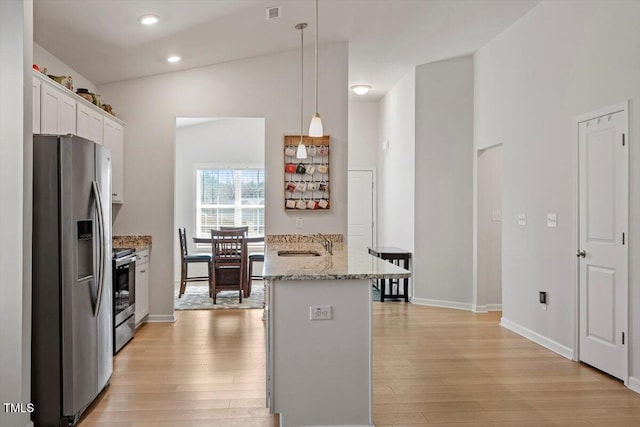 kitchen with stainless steel appliances, hanging light fixtures, light wood-style flooring, white cabinetry, and a sink