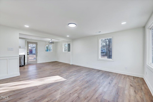 unfurnished living room with plenty of natural light, an inviting chandelier, and light hardwood / wood-style floors