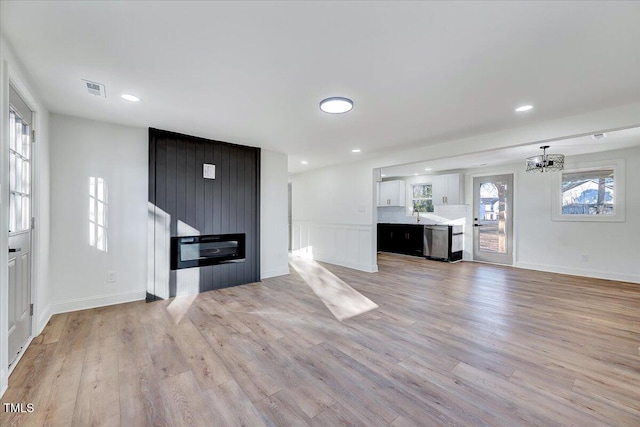 unfurnished living room with sink, a large fireplace, light hardwood / wood-style flooring, and a chandelier