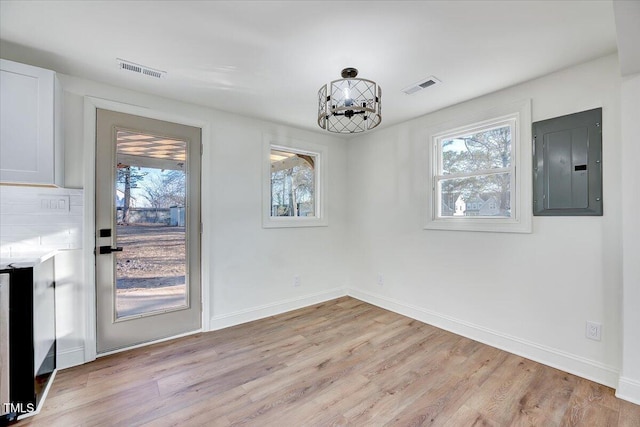 unfurnished dining area featuring a wealth of natural light, an inviting chandelier, light hardwood / wood-style floors, and electric panel