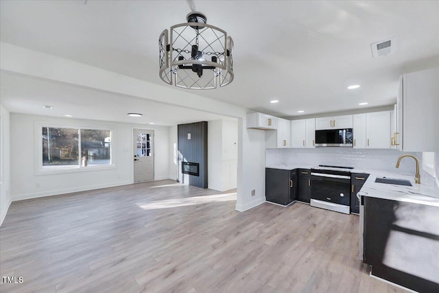 kitchen with white cabinets, stainless steel appliances, tasteful backsplash, sink, and light wood-type flooring