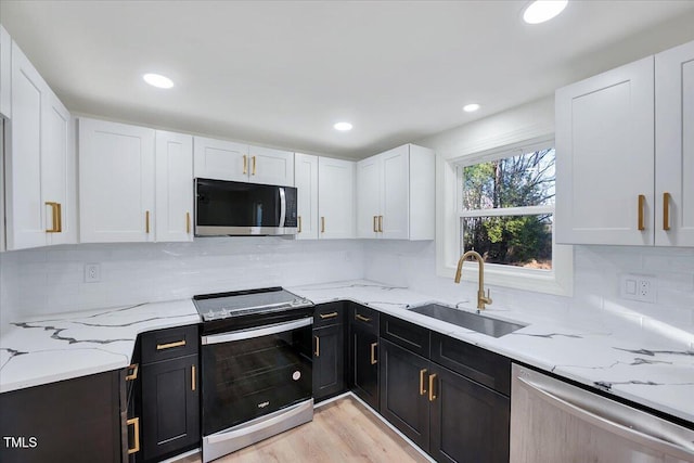 kitchen featuring sink, light wood-type flooring, stainless steel appliances, white cabinets, and light stone counters