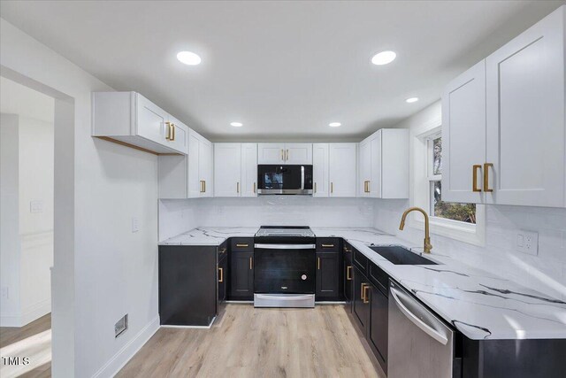 kitchen featuring light stone countertops, appliances with stainless steel finishes, white cabinetry, light hardwood / wood-style floors, and sink