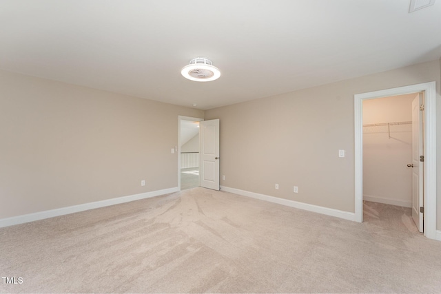 unfurnished bedroom with a walk in closet, a closet, and light carpet