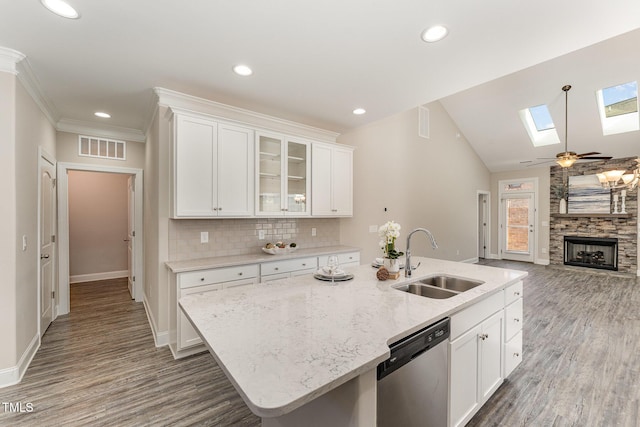 kitchen featuring a stone fireplace, decorative backsplash, white cabinets, stainless steel dishwasher, and sink