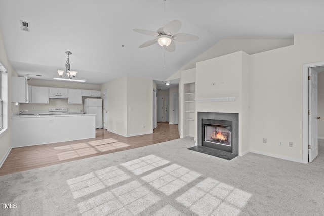 unfurnished living room with vaulted ceiling, ceiling fan with notable chandelier, and light colored carpet