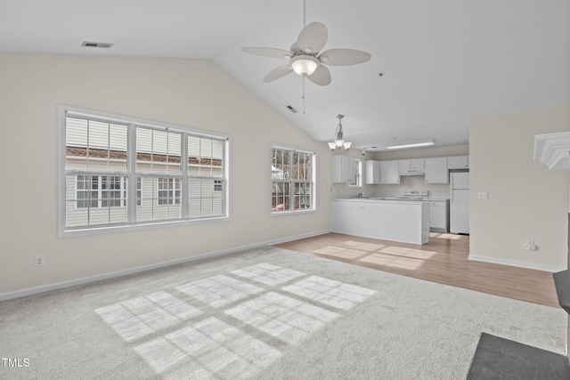 unfurnished living room with vaulted ceiling, ceiling fan with notable chandelier, sink, and light carpet