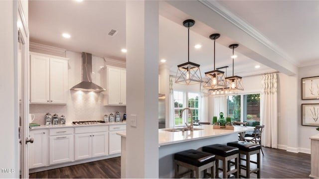 kitchen with stainless steel gas stovetop, white cabinets, wall chimney range hood, sink, and decorative backsplash