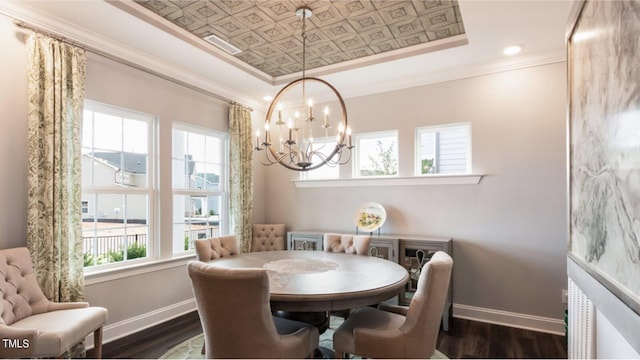 dining area with a chandelier, ornamental molding, dark wood-type flooring, and a tray ceiling