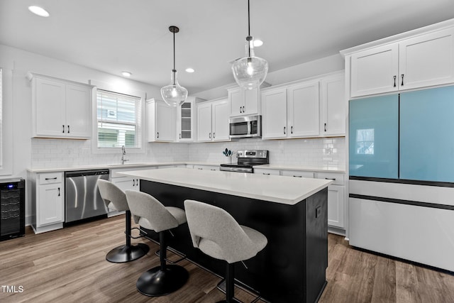 kitchen featuring sink, appliances with stainless steel finishes, a kitchen island, pendant lighting, and white cabinets